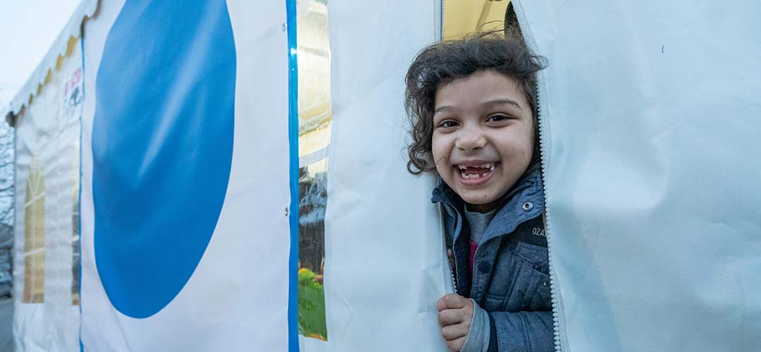 Child laughs while peeking out of the Mother and Child tent at the UNICEF-supported Blue Dot center
